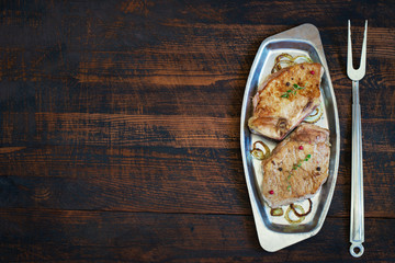 Roasted meat on a metal plate and fork. Top view with copy space
