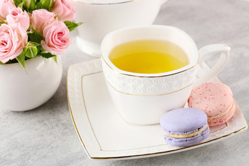 Cup of tea with macaroons and roses on wooden table