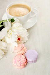 Cup of coffee with macaroons and peonies on wooden table