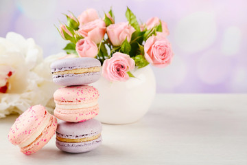 Tasty macaroons with roses and peonies on wooden table