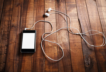 Black smartphone with a blank screen and headphones. Mobile phone with headphones on an old wooden table background.