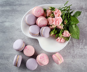 Tasty macaroons with roses on table