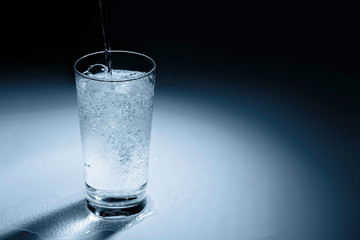 Pouring water into glass on blue background