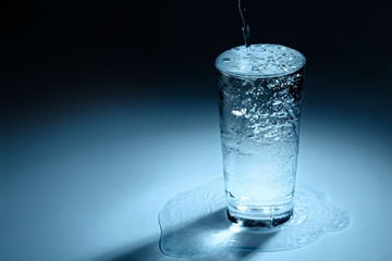 Pouring water into glass on blue background