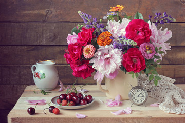 Still life with a summer bouquet, berries and alarm clock.
