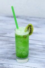 Kiwi smoothie with ice in a glass with straws on wood background