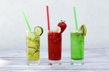 Three glasses of summer drinks with ice on wood background