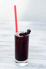 Blackcurrant lemonade in a glass with ice on wood background