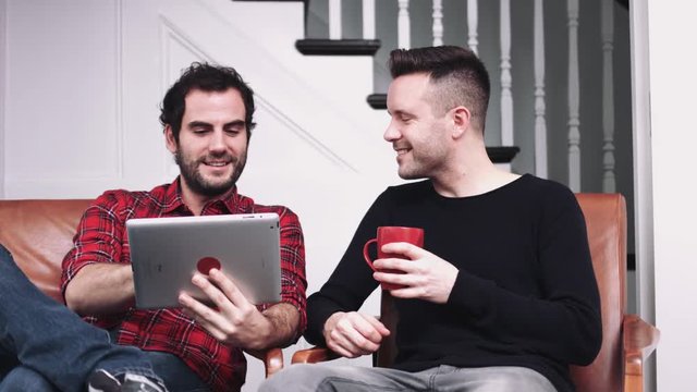 Same sex couple watching pictures on digital tablet and drinking coffee