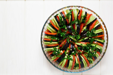 Raw Ratatouille with eggplants, tomatoes and zucchini decorated basil leaves on white wooden background