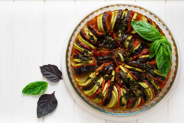 Ratatouille with eggplants, tomatoes and zucchini decorated basil leaves on white wooden background