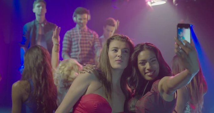 Female friends taking self photograph with mobile phone while enjoying music in nightclub