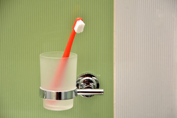 Toothbrush in glass in metal holder fixed to green tile at wall in bathroom
