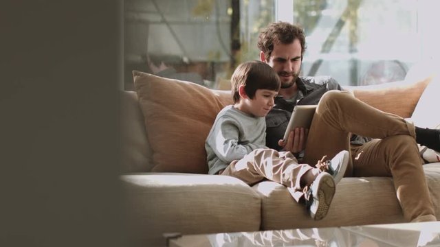 Father and son on the couch using digital tablet