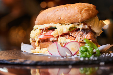 A hamburger consisting of fish, omelets and vegetables served on a stone Board