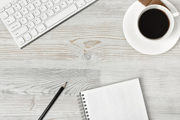 Workplace with cup of coffee, keyboard, smarthphone, white sheets and pen on wooden surface in top view.