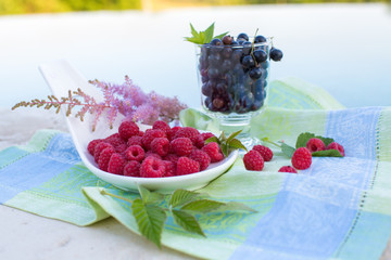 black currants in a glass and raspberries on leaves on the background of the pool and green napkins