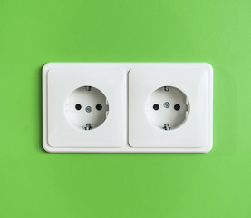Two white electrical power sockets on a green wall