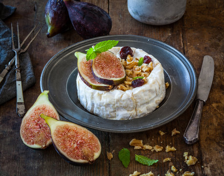 Camembert cheese with fresh figs, walnuts, raisins and honey. Rustic retro vintage ambiance.