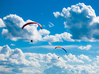 Two dark paraglide silhouettes on background of blue summer sky and white clouds. Adrenalin sport...