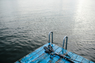 fishing rods and slippers lay on the pier near the water