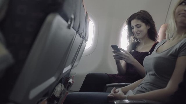 Young adult women on airplane with mobile phone