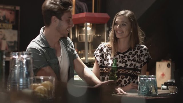 Man holding beer bottle and talking with female friend while enjoying in bar