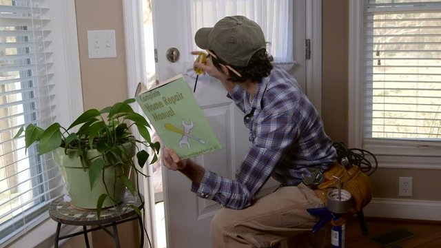 A handyman attempts to fix a broken lock with a repair manual