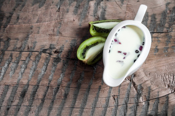Yogurt with strawberry slices and blueberries on a wooden board - near the yogurt lie kiwi slices