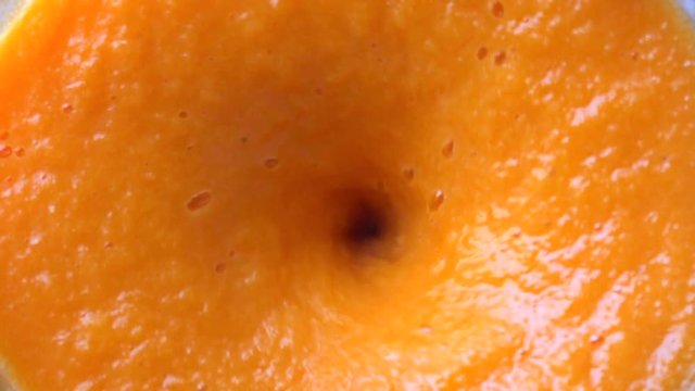 Slow motion close up shot of orange smoothie being made in a blenter. Top view