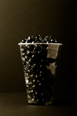 Currant berries in a plastic glass on black background. Toned