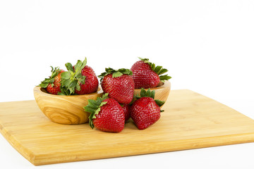 Strawberries arranged on a cutting board with two wooden bowls and a white background