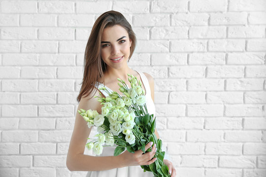Beautiful young woman holding bouquet on white brick wall background