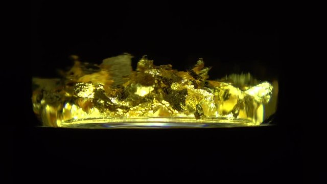 Close up of gold flakes in flask turning around on pedestal lighting underneath chemical element symbol Au because of softness of pure 24k karat gold usually alloyed with base metals for jewelry 4k