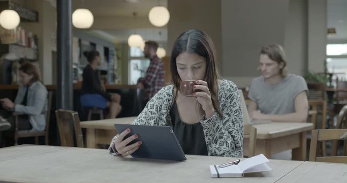 Woman using tablet and drinking coffee in pub