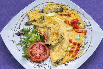 Omlette with herbs,vegetables and cheese in a plate on wooden table.