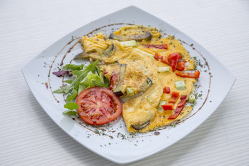 Omlette with herbs,vegetables and cheese in a plate on wooden table.