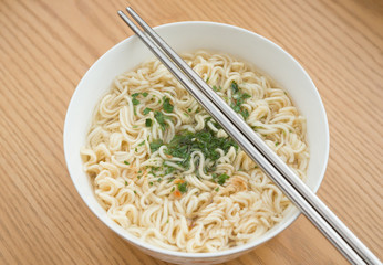 bowl of instant noodles with sauce and chopsticks on a wood table
