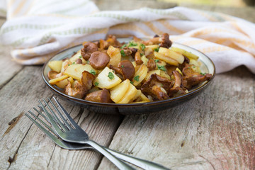 fried young potatoes with chanterelles mushrooms in bowl on old