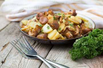 fried young potatoes with chanterelles mushrooms in bowl on old