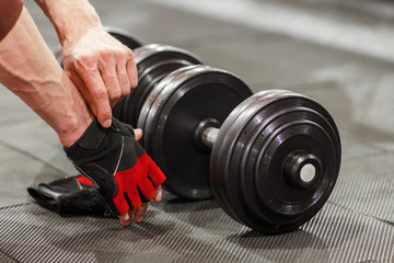 Man put on sport gloves before flexing dumbbells. Male athlete preparing for pumping iron at gym. Weightlifting training preparation