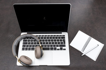 Laptop on a desk with headphones and a notepad
