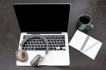 Laptop on a desk with headphones, a notebook and steaming coffee