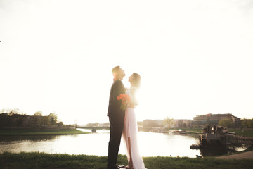Elegant beautiful wedding couple posing near river at sunset