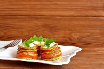 Fried zucchini with fresh tomatoes, yoghurt and green parsley. Delicious vegetable appetizer on plate and on wooden background. Easy zucchini snacking for summer