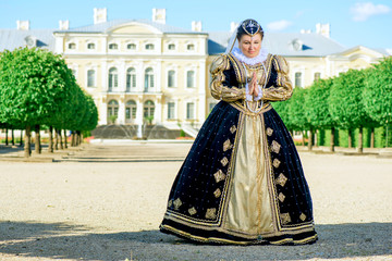 Fototapeta na wymiar Historical cosplay. Beautiful woman in the similitude of Marguerite of Navarre, queen of France ancient dress in the garden near palace