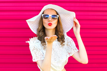 Woman in summer straw hat sends an air kiss over colorful pink b