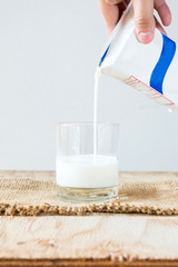 Hand holding a carton of milk poured into a glass on white backg