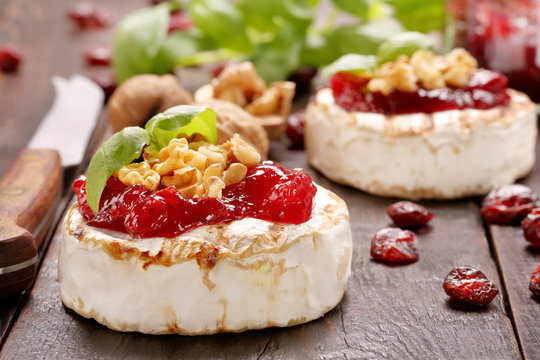 Grilled brie cheese with cranberry jam and walnuts on old wooden