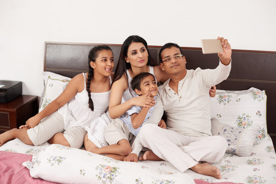 Happy Indian family taking selfie together in bed